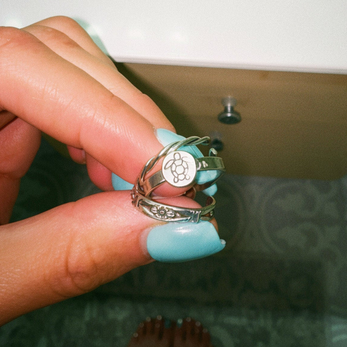 Hand holding a silver ring with a blue gemstone on a bathroom counter.