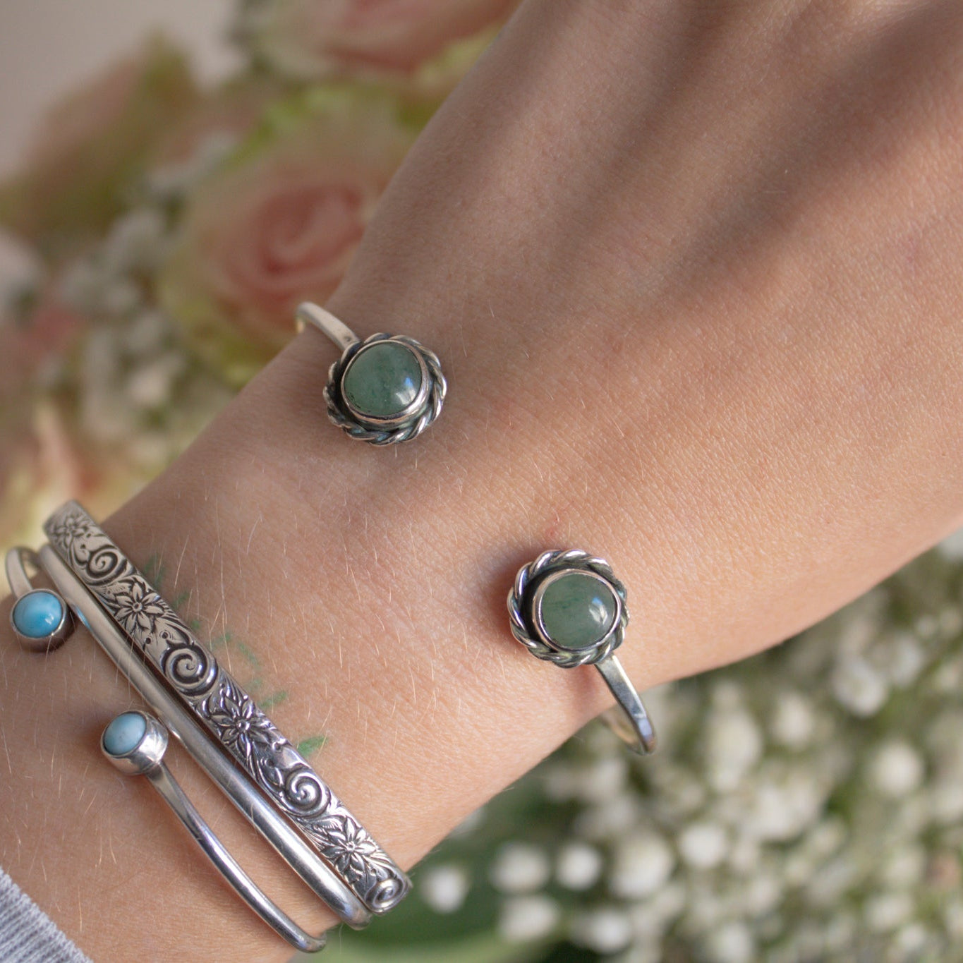 Silver bracelets with green stones on a wrist against a floral background
