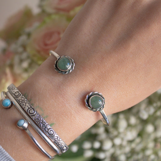 Silver bracelets with green stones on a wrist against a floral background
