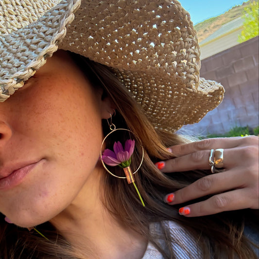 Woman wearing a straw hat, floral earring, and ring outdoors.