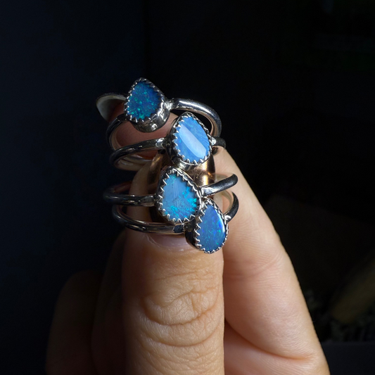 Three blue gemstone rings stacked on a finger against a dark background